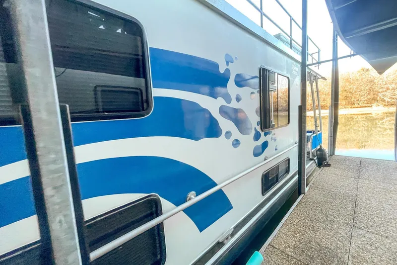 Slide: The Image of 1996 Lakeview 66 x 16 Widebody Houseboat with blue wave design docked by the lake. - 8