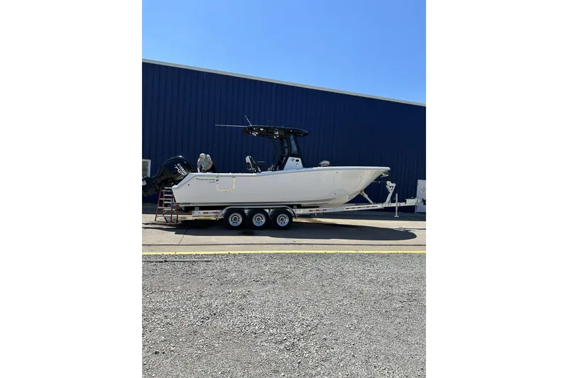 The Image of 2024 Tidewater 272 CC Adventure boat on trailer, parked outside a blue building. - 0