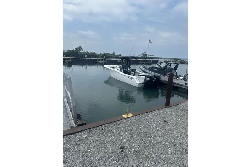 Slide: The Image of 2024 Tidewater 272 CC Adventure boat docked in a marina under a cloudy sky. - 2