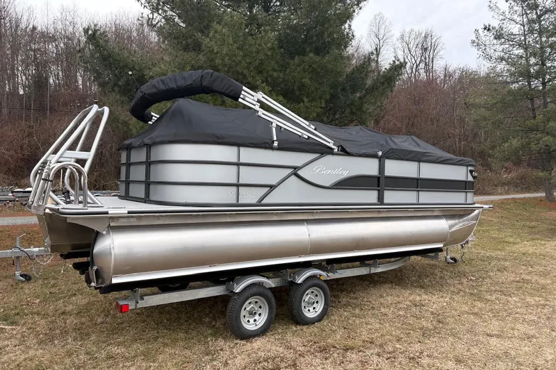 Slide: The Image of 2026 Bentley Pontoons Legacy 223 Navigator on trailer, covered, in wooded area. - 3