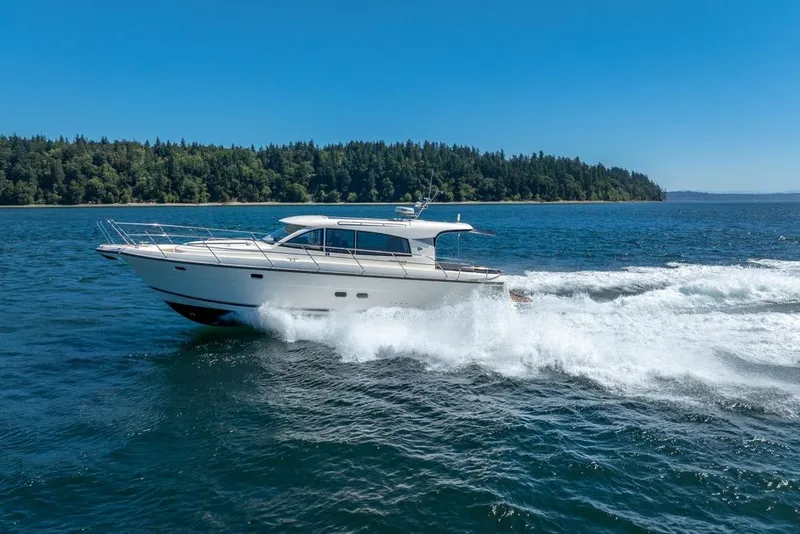 Slide: The Image of 2022 Nimbus 405 Coupé cruising on a sunny day, surrounded by blue water and lush forest. - 2