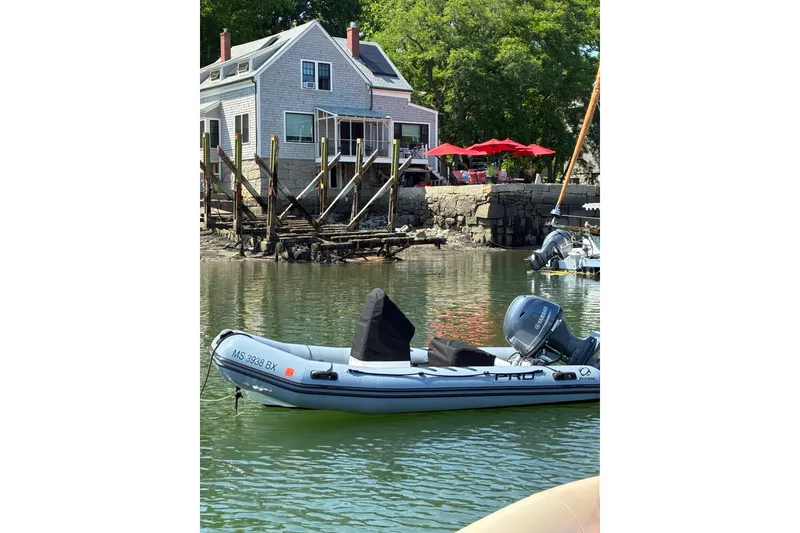 Slide: The Image of 2023 Zodiac Pro Classic 420 boat moored near a waterfront house with red umbrellas. - 1