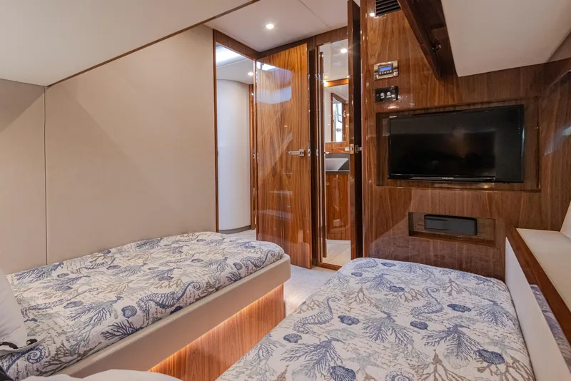 Slide: The Image of 2017 Riviera Sport Cruiser cabin with twin beds, wood paneling, and a wall-mounted TV. - 34