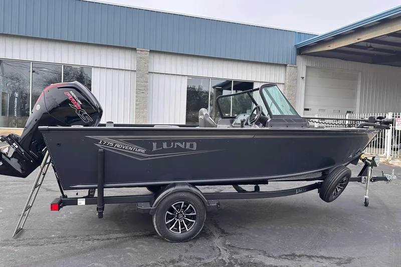 The Image of 2026 Lund 1775 Adventure Sport boat on trailer, parked outside industrial building. - 0