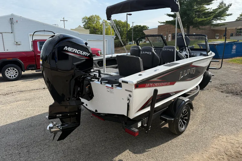 Slide: The Image of 2026 Lund 1875 Crossover XS boat with Mercury engine, parked outdoors. - 5