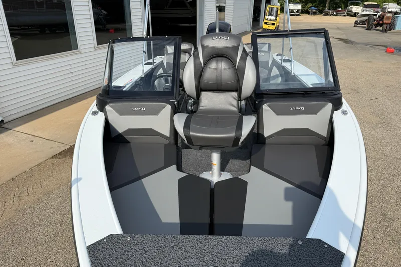 Slide: The Image of 2026 Lund 1875 Crossover XS boat interior with seating and windshield, parked outdoors. - 9