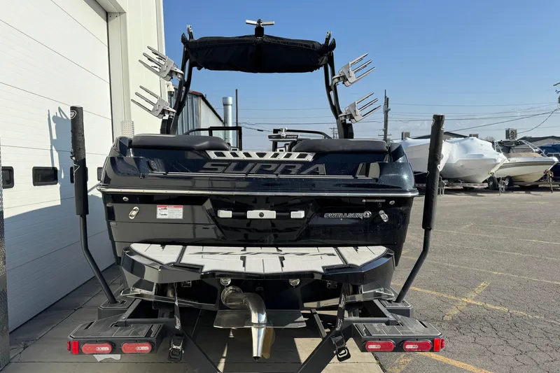 Slide: The Image of 2021 Supra SL 575 boat rear view, parked outdoors near other boats. - 2