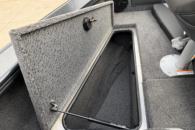 Slide: The Image of 2026 Lund 1875 Crossover XS boat storage compartment with open lid and carpeted interior. - 11
