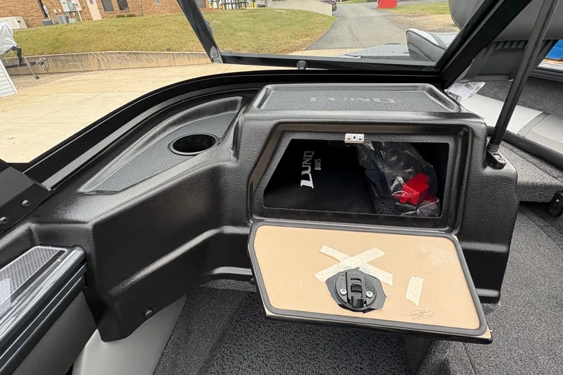 Slide: The Image of 2026 Lund 1875 Crossover XS boat interior with open storage compartment and cup holder. - 20