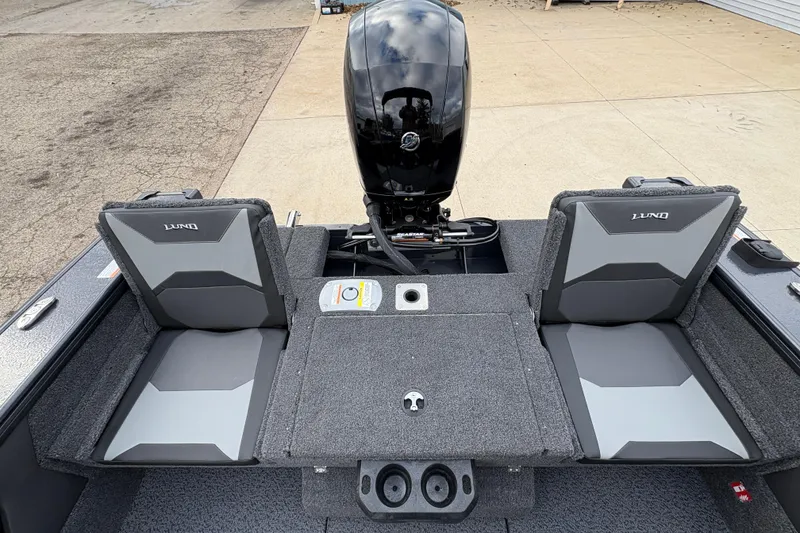 Slide: The Image of 2026 Lund 1875 Crossover XS boat interior with seating and motor, docked on concrete. - 25