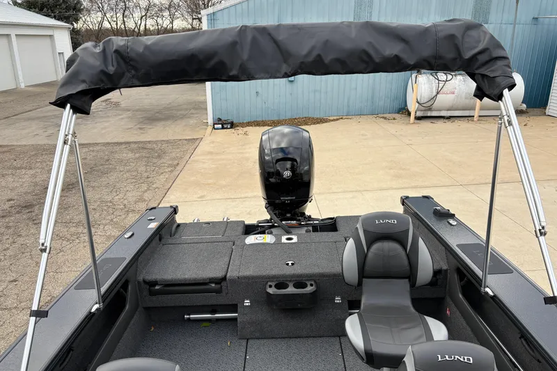 Slide: The Image of 2026 Lund 1875 Crossover XS boat interior with seating and motor, docked outdoors. - 28