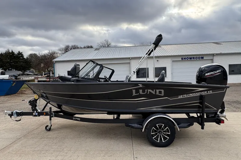Slide: The Image of 2026 Lund 1875 Crossover XS boat on trailer, parked outside showroom. - 5