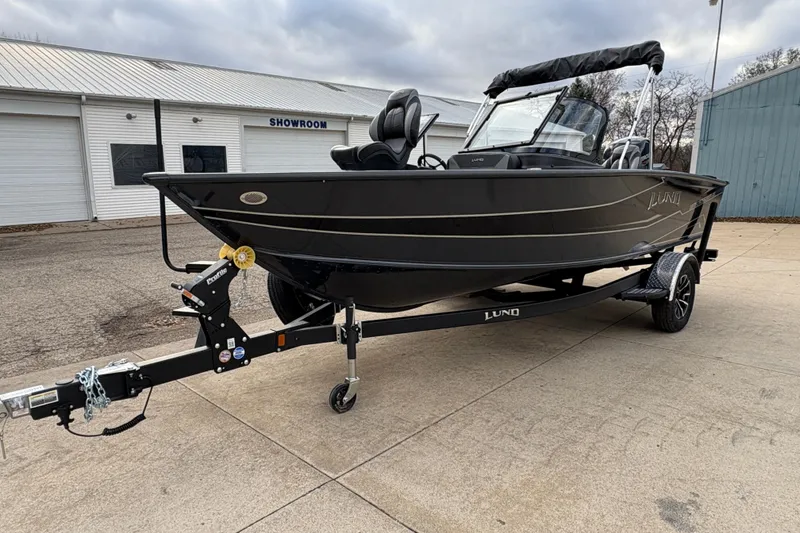 Slide: The Image of 2026 Lund 1875 Crossover XS boat on trailer outside showroom, overcast sky. - 6