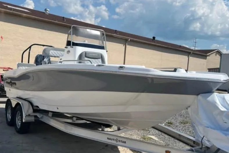 Slide: The Image of 2026 NauticStar 211 Hybrid boat on trailer, parked outdoors under a cloudy sky. - 2