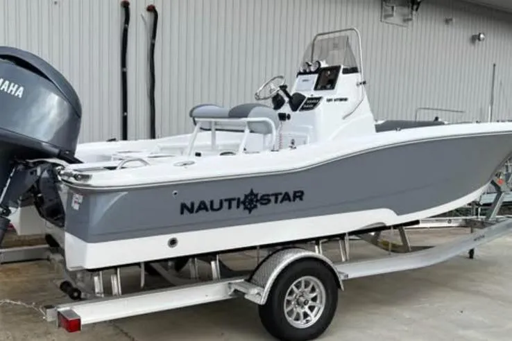 Slide: The Image of 2026 NauticStar 191 Hybrid boat on trailer, featuring Yamaha engine, parked outdoors. - 2