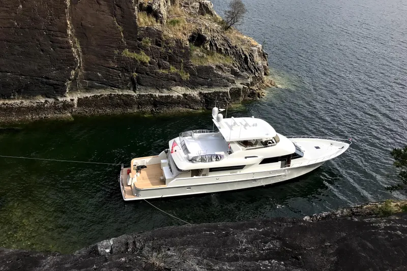 Slide: The Image of 2006 NorthCoast PILOTHOUSE yacht anchored near rocky cliff in serene waters. - 2