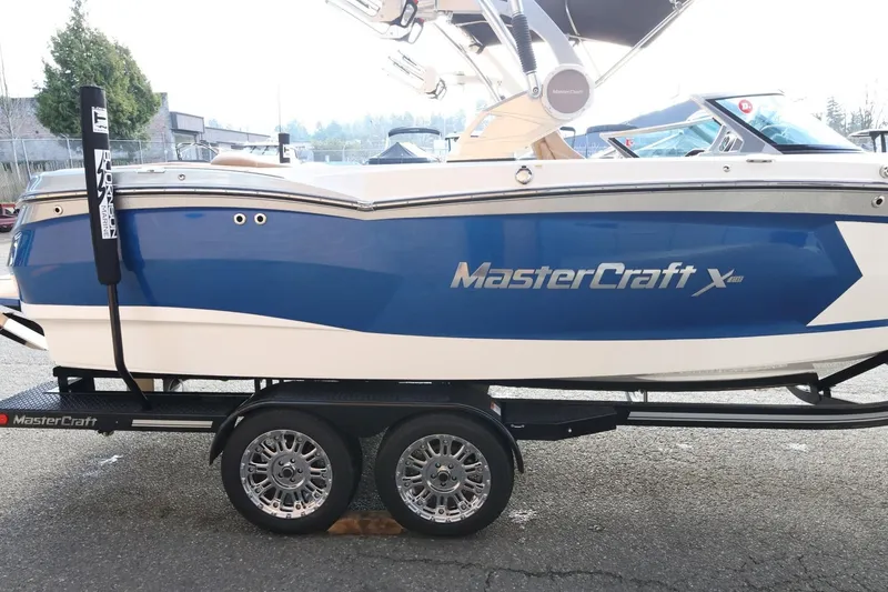 Slide: The Image of 2020 MasterCraft XStar boat on trailer, blue and white design, parked outdoors. - 5