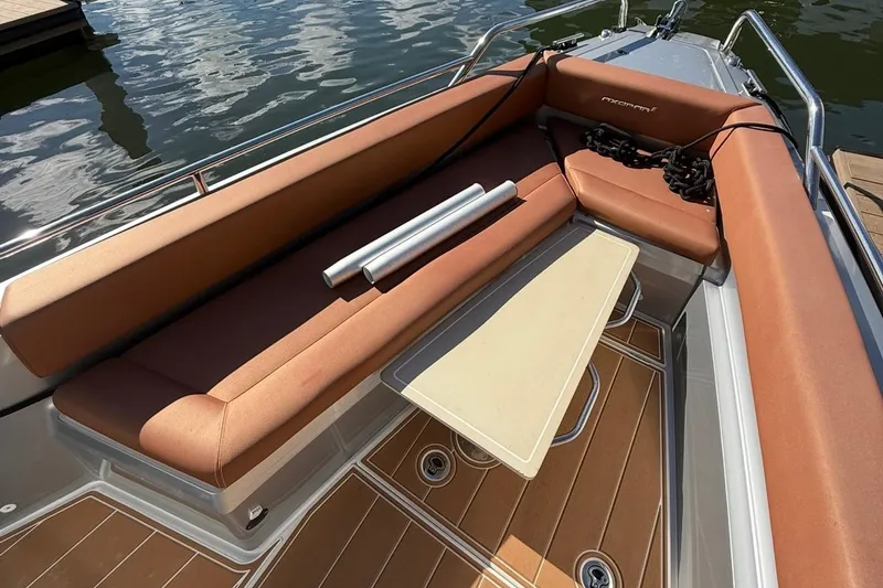 Slide: The Image of 2019 Axopar 28 Cabin boat interior with brown seating and table, docked by water. - 17