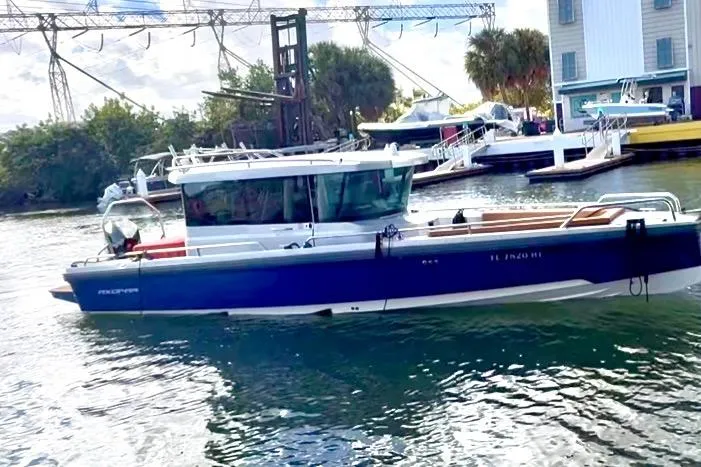 Slide: The Image of 2019 Axopar 28 Cabin boat docked in a marina with surrounding boats and trees. - 2