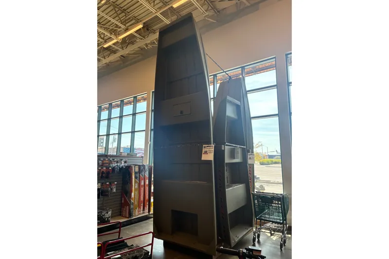The Image of 2026 Tracker Grizzly 15 Jon boat displayed vertically in a store with large windows. - 0