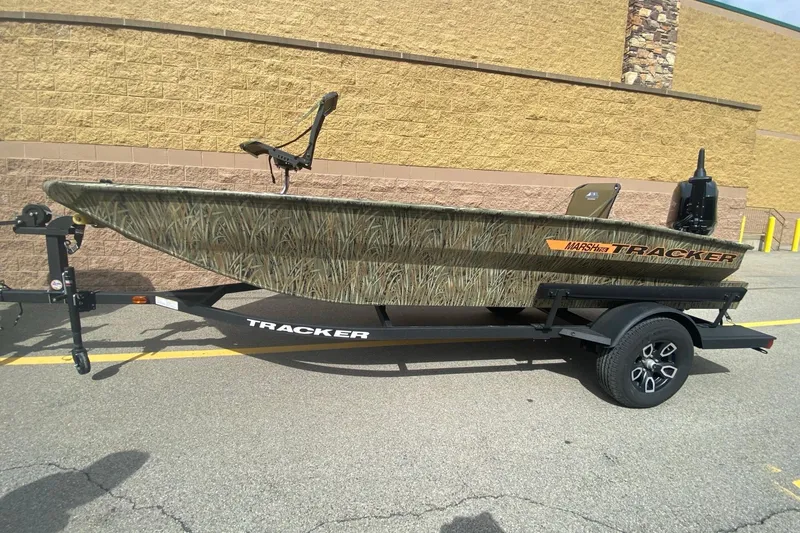 The Image of 2026 Tracker Grizzly 1756 T Marsh boat on trailer, camo design, parked outdoors. - 0