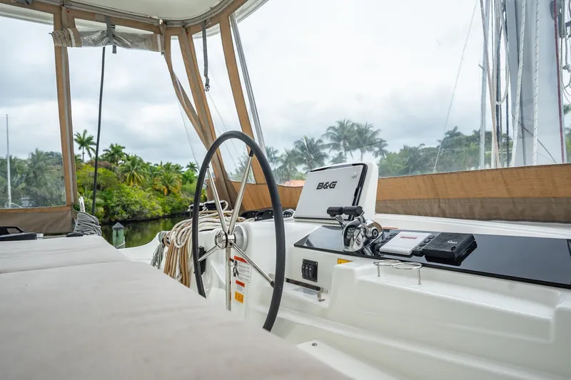 Slide: The Image of 2022 Lagoon 46 yacht cockpit with steering wheel and navigation equipment, surrounded by lush greenery. - 132