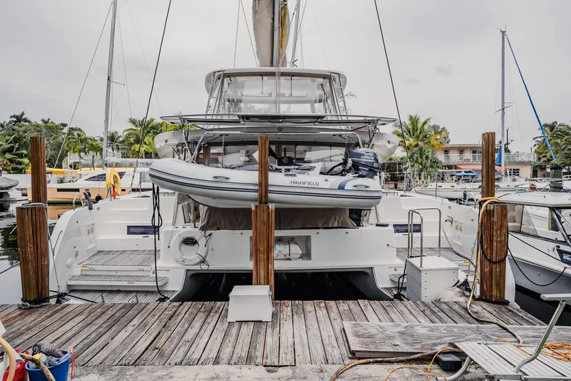 Slide: The Image of 2022 Lagoon 46 catamaran docked with inflatable boat on davits, marina background. - 163