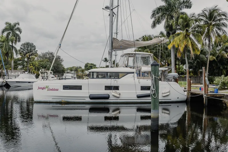 Slide: The Image of 2022 Lagoon 46 catamaran "Jungle Goddess" docked by palm trees, reflecting on calm water. - 63