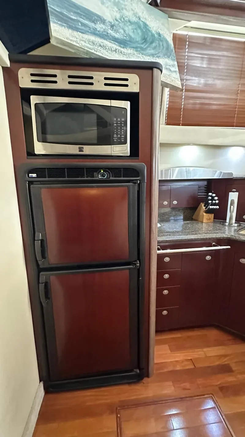 Slide: The Image of 2006 Sea Ray 44 Sedan Bridge kitchen with microwave, fridge, and wooden cabinetry. - 15