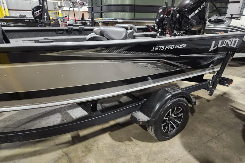 Slide: The Image of 2024 Lund 1875 Pro Guide boat on trailer in a warehouse setting. - 1