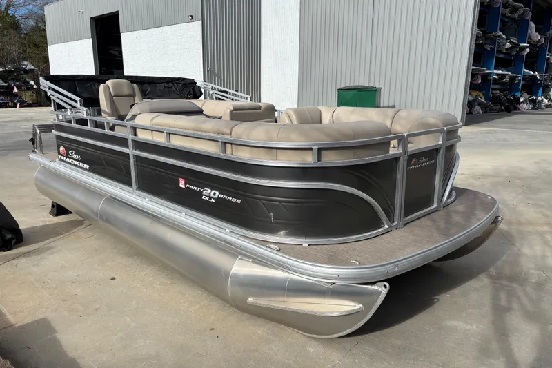 The Image of 2024 Sun Tracker Party Barge 20 DLX pontoon boat with beige seating, parked outdoors. - 0