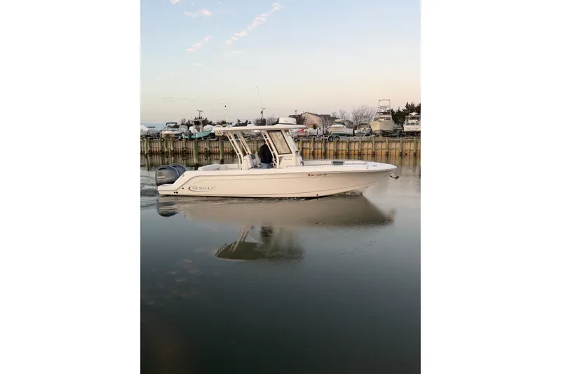 Slide: The Image of 2020 Robalo R272 Center Console boat on calm water near a dock. - 2