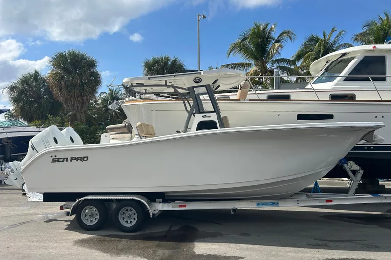 Slide: The Image of 2026 Sea Pro 262 Offshore boat on trailer, surrounded by palm trees and other boats. - 2