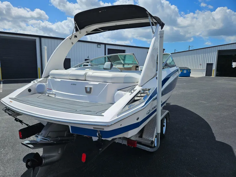 Slide: The Image of 2014 Regal 2100 Bowrider boat on trailer, parked outdoors under a blue sky. - 4