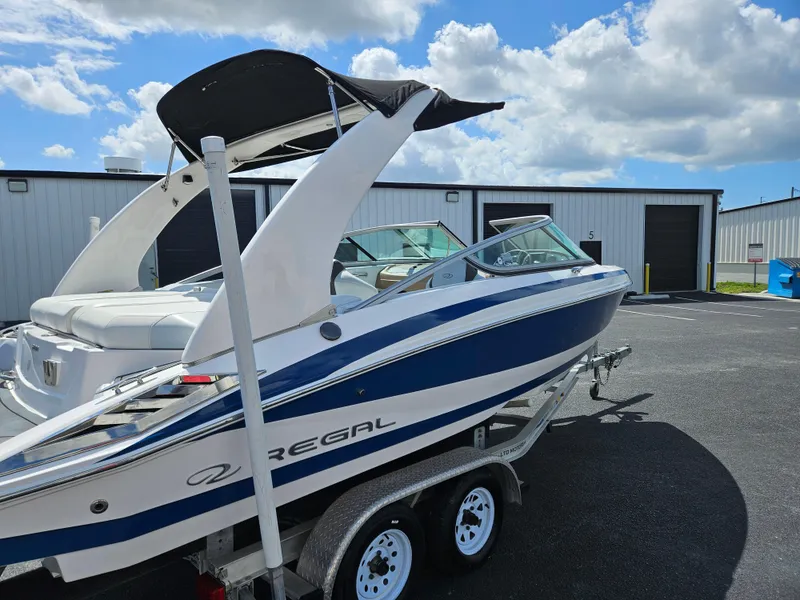 Slide: The Image of 2014 Regal 2100 Bowrider boat on a trailer, parked outdoors under a blue sky. - 5