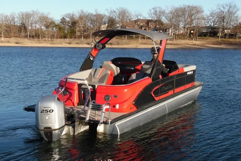 Slide: The Image of 2023 Manitou 25 XT RFX pontoon boat on a serene lake. - 2