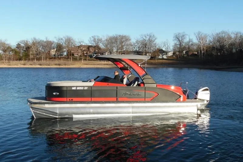 Slide: The Image of 2023 Manitou 25 XT RFX pontoon boat on a calm lake, with trees in the background. - 8