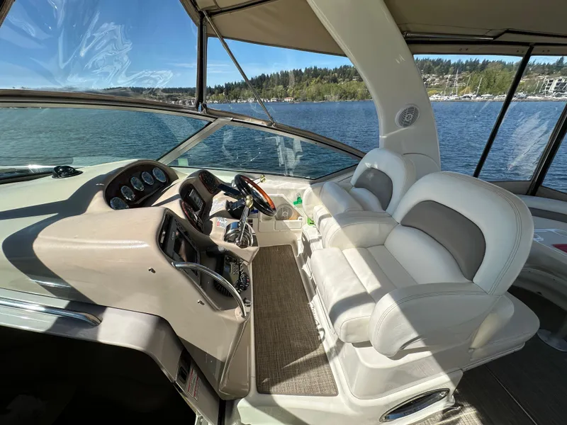 Slide: The Image of 2004 Sea Ray 340 Sundancer helm with dual seats, overlooking serene lake and forested shoreline. - 24