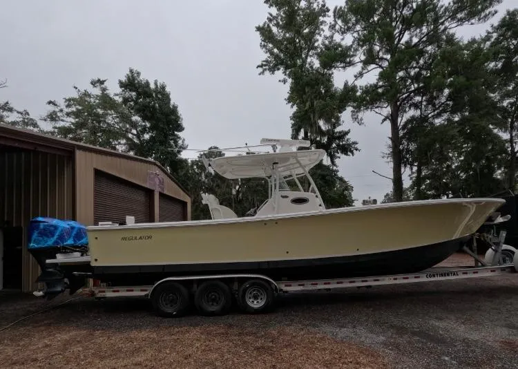Slide: The Image of 2013 Regulator 34 Center Console boat on trailer near trees and building. - 7