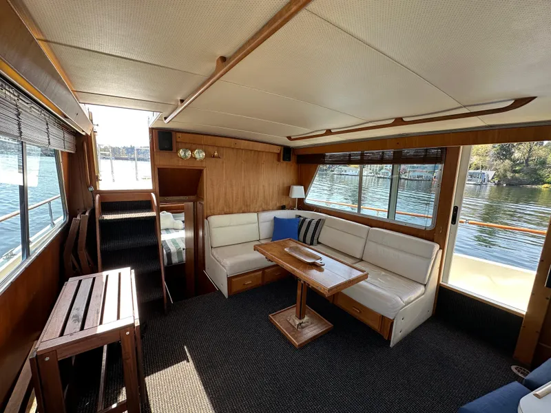 Slide: The Image of 1982 Tollycraft Tri Cabin interior with cozy seating, wooden table, and large windows overlooking water. - 27