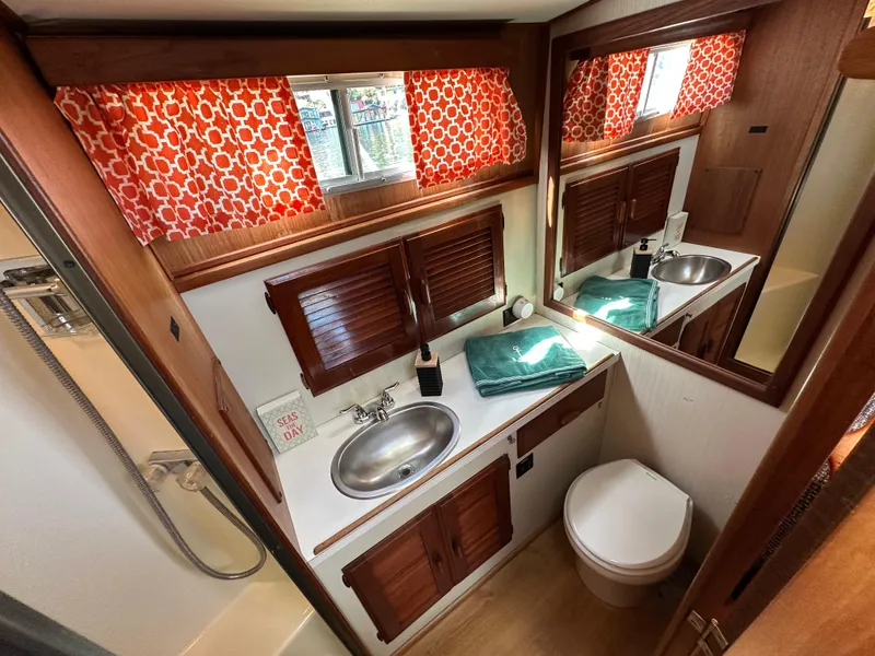 Slide: The Image of 1982 Tollycraft Tri Cabin bathroom with sink, toilet, mirror, and red-patterned curtains. - 42