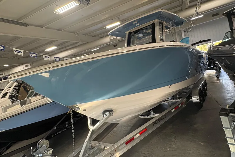 Slide: The Image of 2026 Robalo R300 Center Console boat in showroom, blue hull, on trailer. - 2