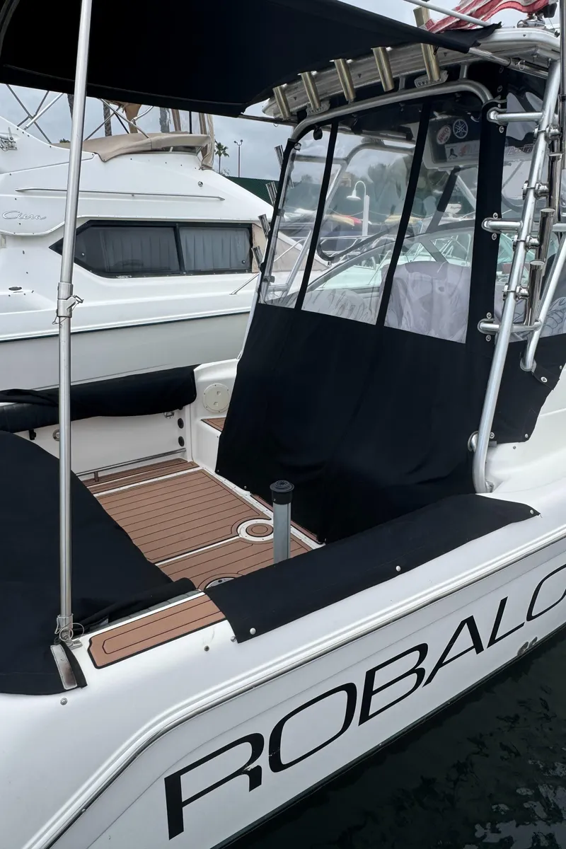 Slide: The Image of 2004 Robalo R265 Walkaround boat with black canopy and seating, docked in a marina. - 2