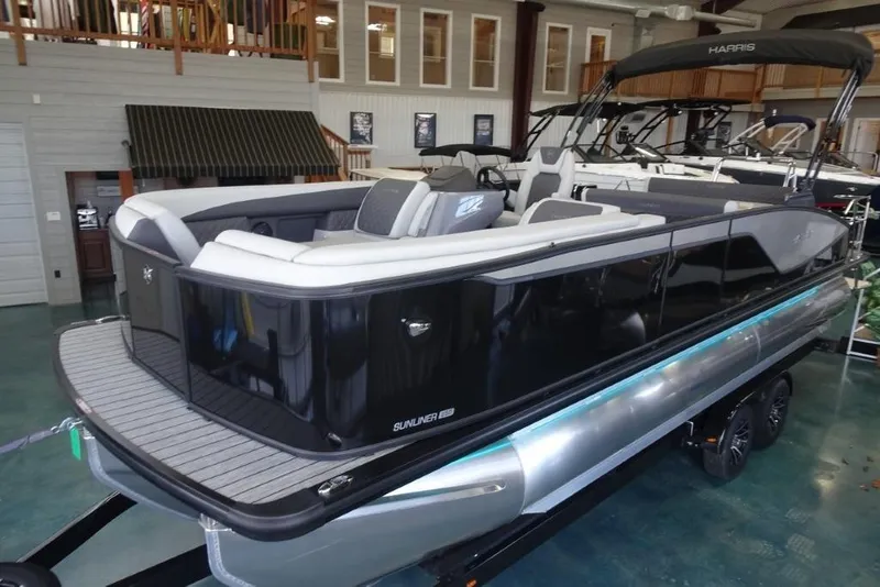 Slide: The Image of 2026 Harris Sunliner 250 pontoon boat in showroom, featuring sleek black design and modern seating. - 10