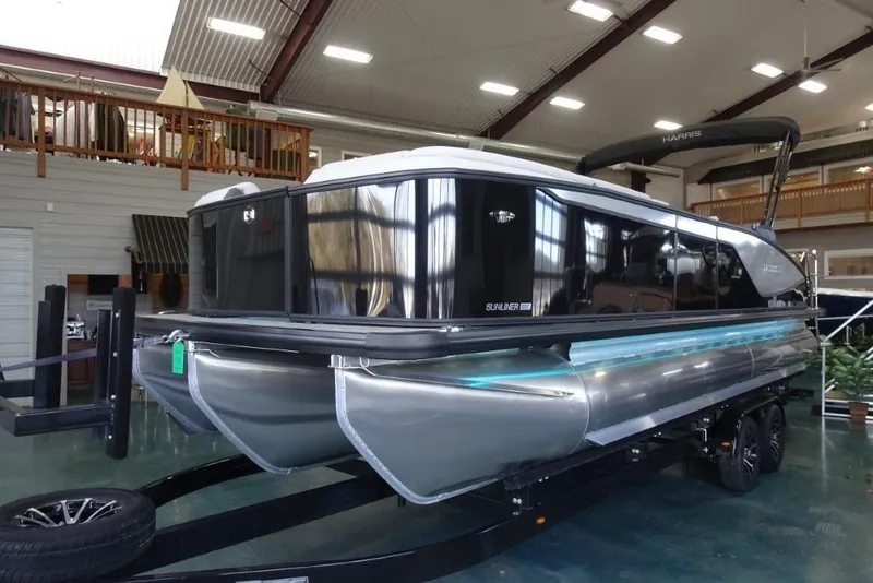 Slide: The Image of 2026 Harris Sunliner 250 pontoon boat displayed indoors on a trailer. - 9
