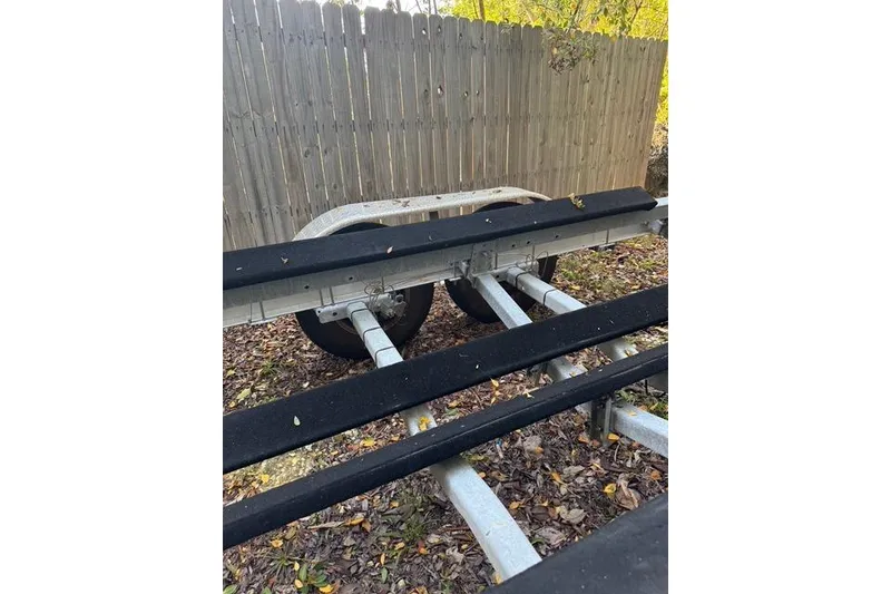 Slide: The Image of Trailer for 2017 Regulator 25 boat, parked on leaf-covered ground near wooden fence. - 44