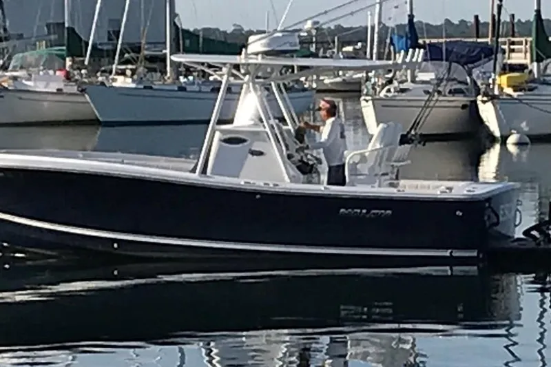 Slide: The Image of 2014 Regulator 25 boat in marina, person steering, surrounded by docked sailboats. - 3