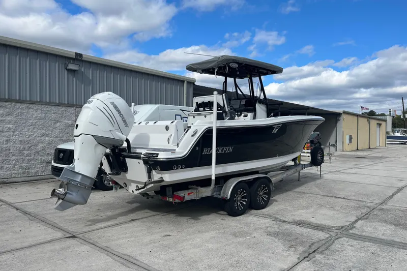 Slide: The Image of 2021 Blackfin 252 CC boat on trailer, parked outdoors near industrial buildings. - 2