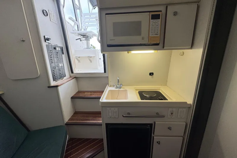 Slide: The Image of Compact kitchen area in a 1995 Pursuit 3000 Express boat, featuring a microwave and stovetop. - 21