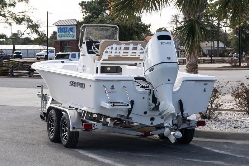 Slide: The Image of 2026 Sea Pro 210 Bay boat on trailer, parked near palm trees and a shop. - 4